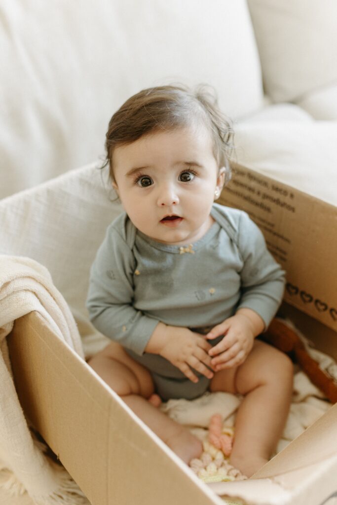 Cute baby girl sitting in a cardboard box, adding a playful charm.