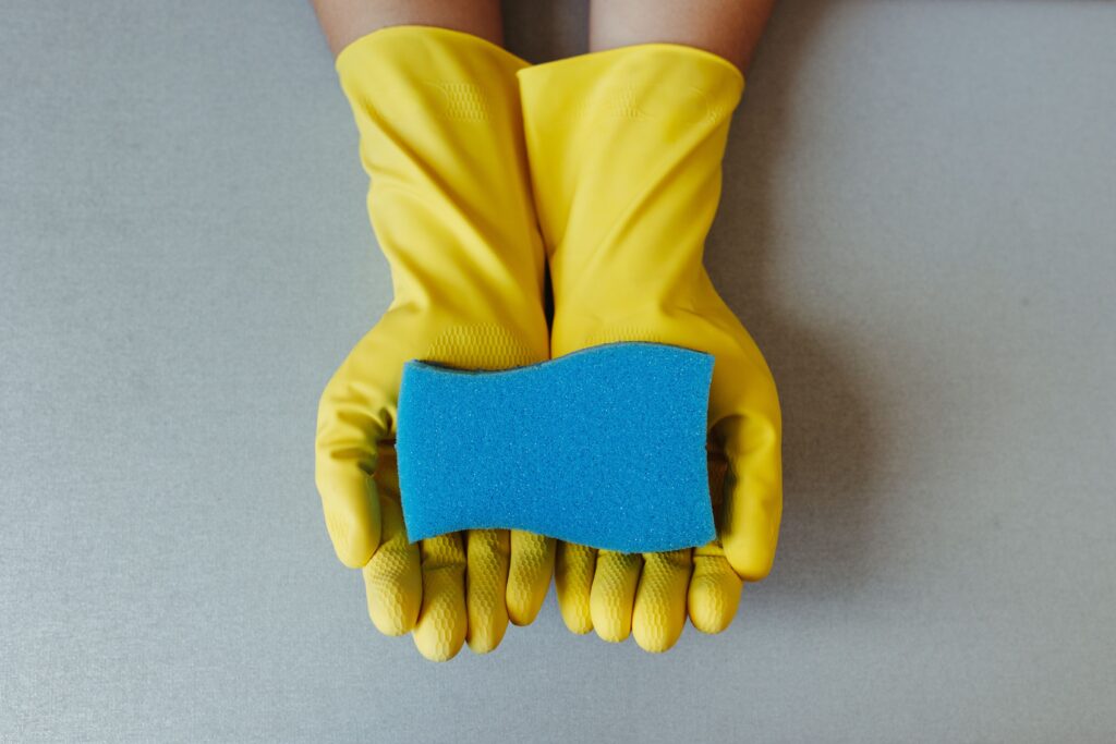 Yellow rubber gloves hold a blue sponge, symbolizing cleaning and hygiene.